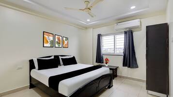 A bedroom with a bed, a ceiling fan, an air conditioning unit, a window with curtains, and artwork on the wall.