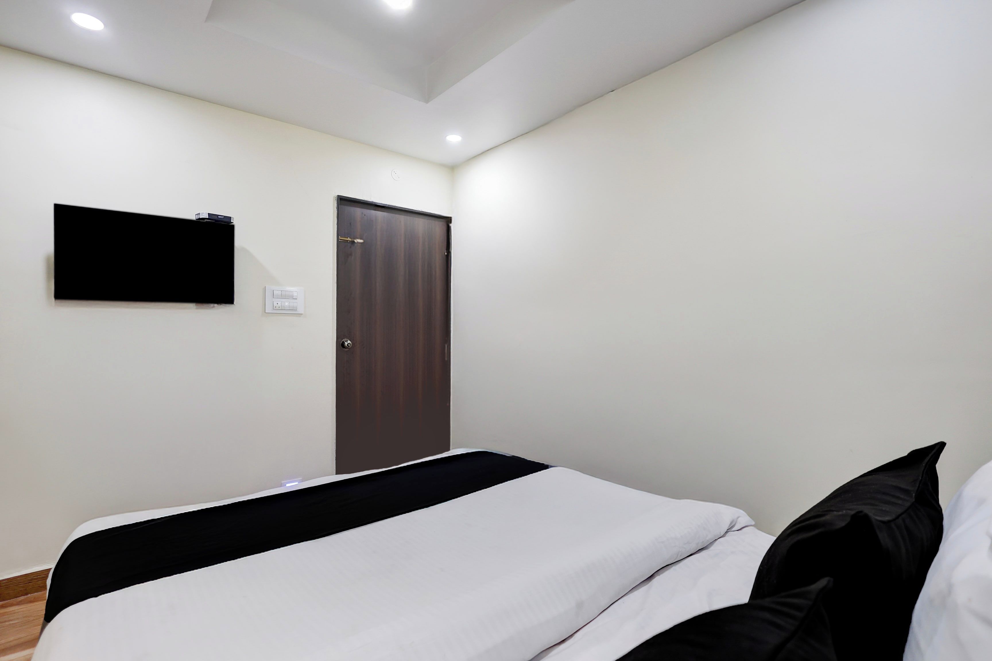 A hotel room with a bed, a flat-screen TV mounted on the wall, and a door.