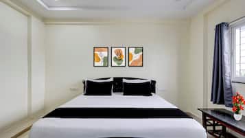 Une chambre d’hôtel avec un lit, un bureau et une fenêtre avec des rideaux. Trois tableaux encadrés sont accrochés au mur.