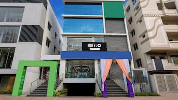 Un hôtel à plusieurs étages, reconnaissable à son grand panneau lumineux indiquant « HÔTEL », un escalier menant à l’entrée et un design architectural moderne.