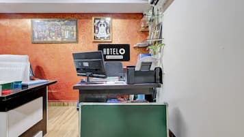 Mostrador de recepción de hotel con computadora, caja registradora y letrero que indica servicios de empresa.