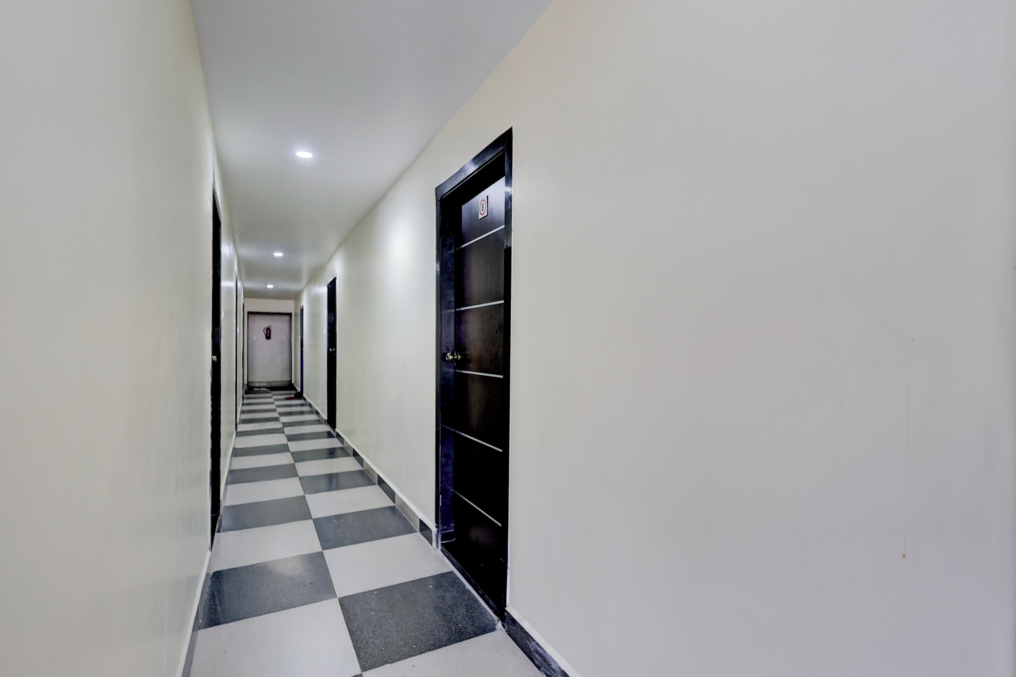 A corridor with a checkered floor, white walls, and doors on both sides.