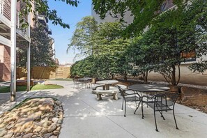 Un espace extérieur aménagé en terrasse, avec des sièges et des tables en pierre, entouré d’arbres et d’un mur en briques.