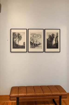 A wall with three framed black and white landscape drawings and a brown leather bench in front. - Street View Condo | Walk to Knoxville’s Best (Knoxville)