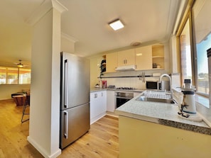 A modern kitchen with stainless steel appliances, a granite countertop, and a view of the outdoors through a large window. - Swell Villa 1 the perfect coastal escape (Kalbarri)