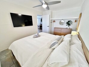A bedroom with a bed, a ceiling fan, a TV mounted on the wall, a wooden dresser, and a mirror. - Swell Villa 1 the perfect coastal escape (Kalbarri)