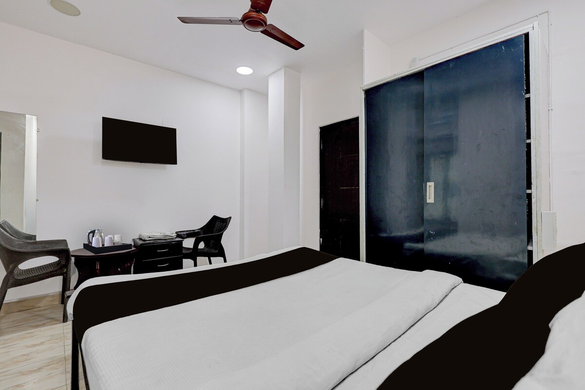 A hotel room with a bed, a desk with chairs, a television, and a ceiling fan.