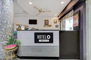 Zona de recepción de hotel con mostrador, ventilador de techo y televisor montado en la pared.