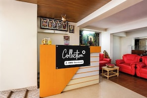 A reception area with a sign reading 'Collector' and 'OYO-Serviced'. There is a wooden reception desk, a red sofa, and a small table with a bowl. The room has a wooden ceiling and tiled flooring.