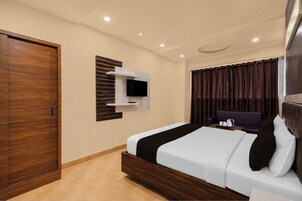 Een moderne hotelkamer met een houten garderobe, een bed met zwart-wit dekbedovertrek, een wandtelevisie en een donkergrijze bank.
