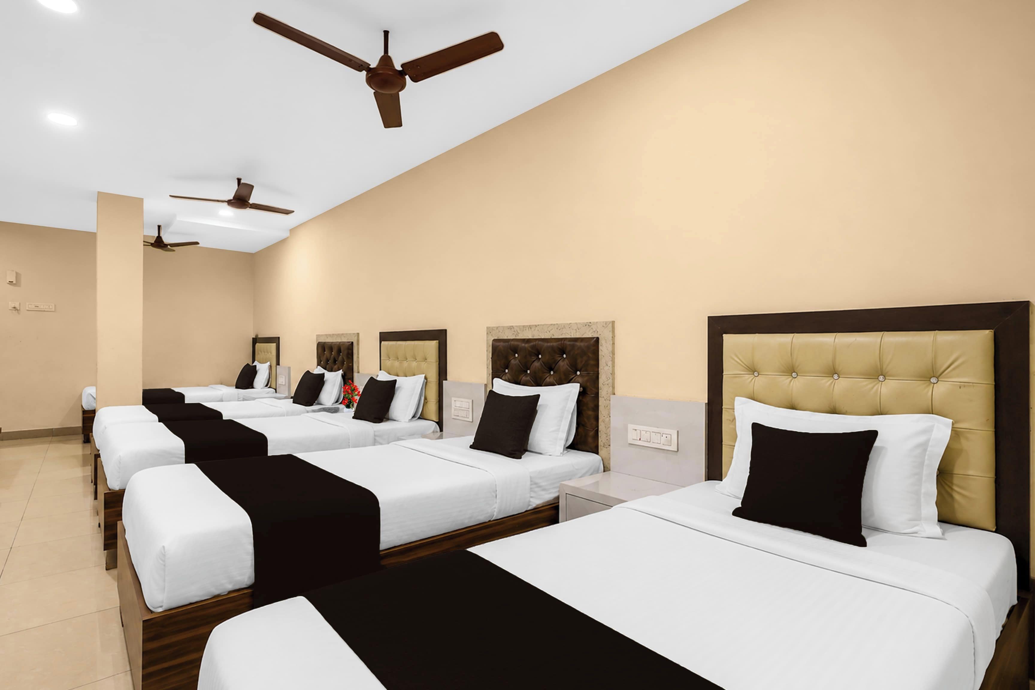 Habitación de hotel con cuatro camas dispuestas en fila, cada una con cabecero y almohadas.