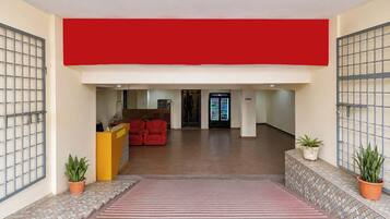 A reception area with a red wall, a reception desk, and a seating area with red chairs. There are potted plants on either side of the reception desk.