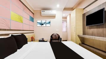 Habitación de hotel con cama, televisión montada en la pared, una silla y una mesita con un jarrón.
