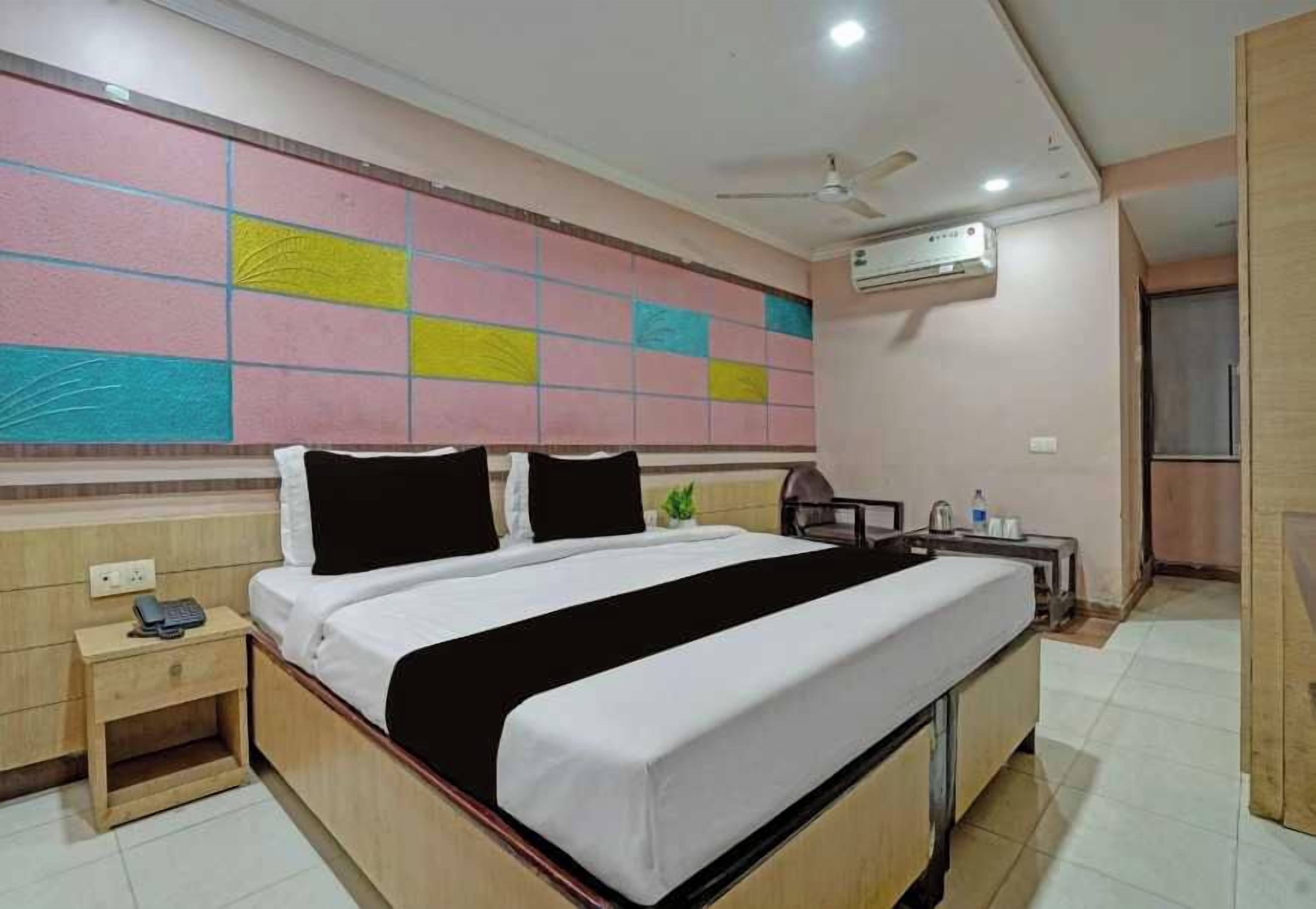 A hotel room with a bed, bedside table, and a wall-mounted air conditioner.