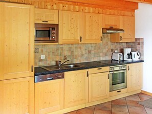 A kitchen with wooden cabinets, a microwave, a coffee maker, and a dishwasher. - Chalet Michelle by Interhome (La Tzoumaz)