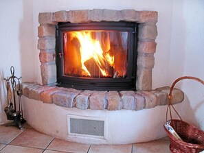 A stone fireplace with a fire burning inside, a metal vent below it, and a wicker basket to the right. - Chalet Michelle by Interhome (La Tzoumaz)