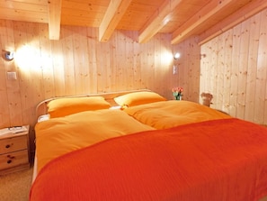 A wooden-paneled room with a bed, a nightstand, and a vase with flowers. - Chalet Michelle by Interhome (La Tzoumaz)
