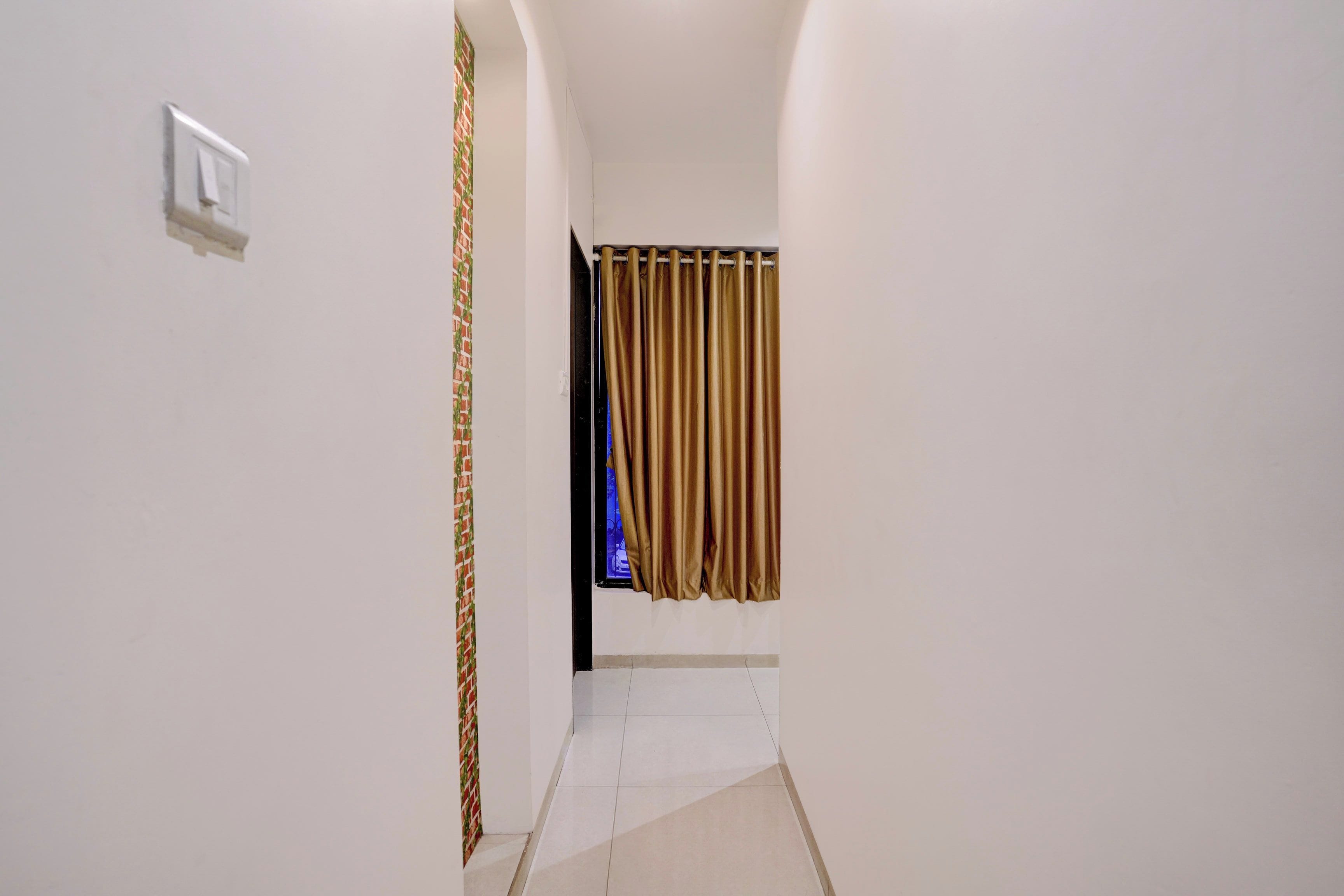 Un pasillo con pared blanca, una puerta con cortina estampada y suelo de baldosas.