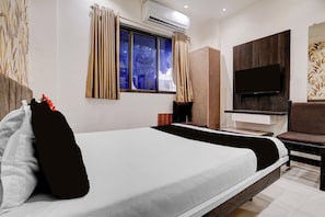 Una habitación de hotel con cama, televisión, ventana con cortinas y equipo de aire acondicionado.