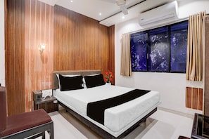 Un dormitorio moderno con una cama grande, una mesita de noche, una silla, un ventanal con cortinas y un equipo de aire acondicionado.