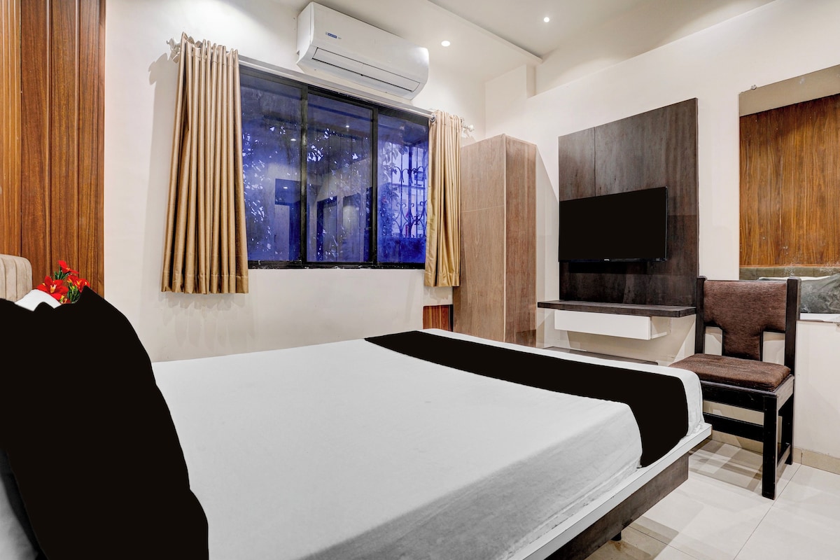 Una habitación de hotel moderna con una cama grande, un televisor de pantalla plana, una zona de estar y un ventanal con cortinas.