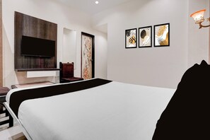 Un dormitorio moderno con una cama grande, un televisor de pantalla plana montado en la pared, una silla y tres obras de arte enmarcadas.