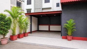 Un espacio al aire libre cubierto con plantas en macetas, suelo de baldosas y un edificio de techo rojo y paredes blancas.