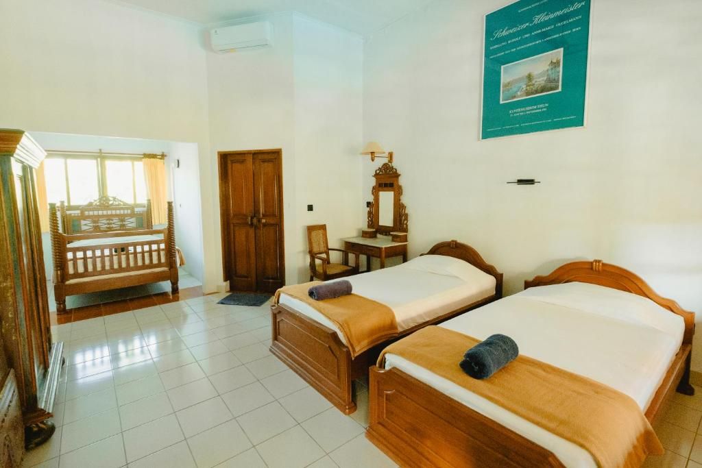 Ein Hotelzimmer mit zwei hölzernen Betten, einer Holzbank, einem Schreibtisch mit Stuhl und einem Wandspiegel.