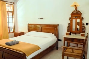 A hotel room with a wooden bed, a nightstand, a desk with a mirror, and a chair.