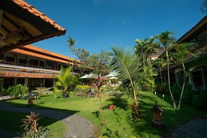 A courtyard with a pathway, palm trees, and a building with a tiled roof.