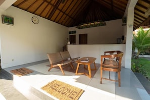 A covered outdoor seating area with two wooden chairs, a small table, and a bench.
