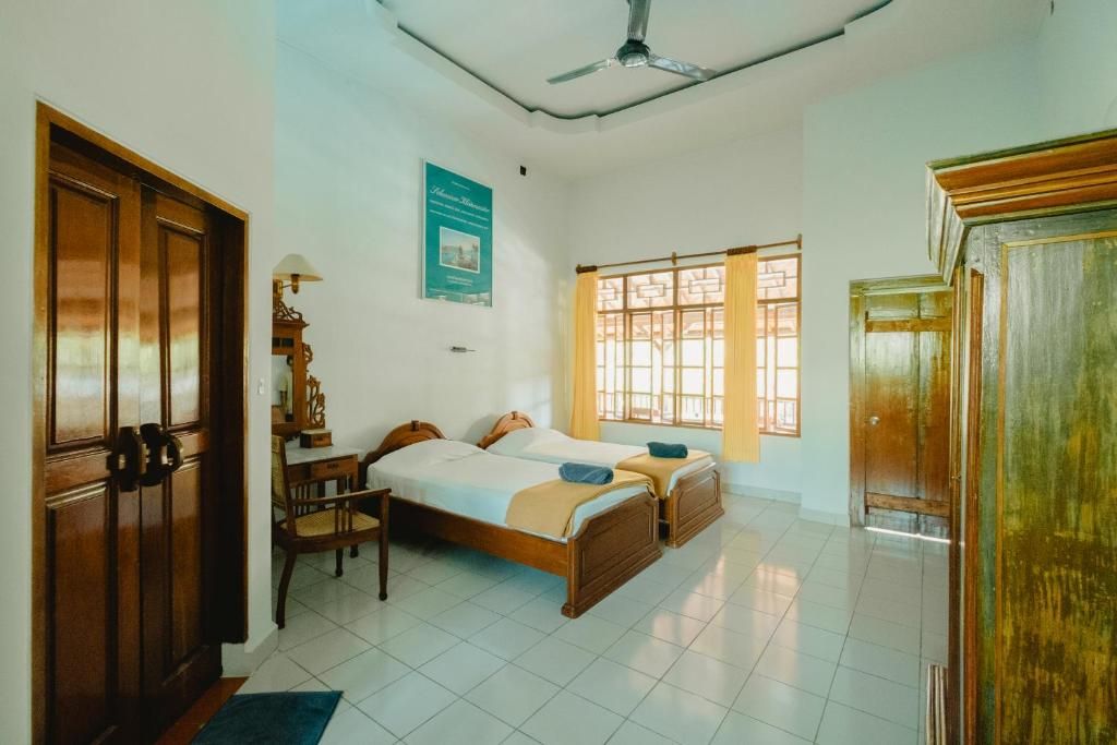 Une chambre avec deux lits, un bureau, une chaise, une fenêtre avec des rideaux et un ventilateur de plafond.