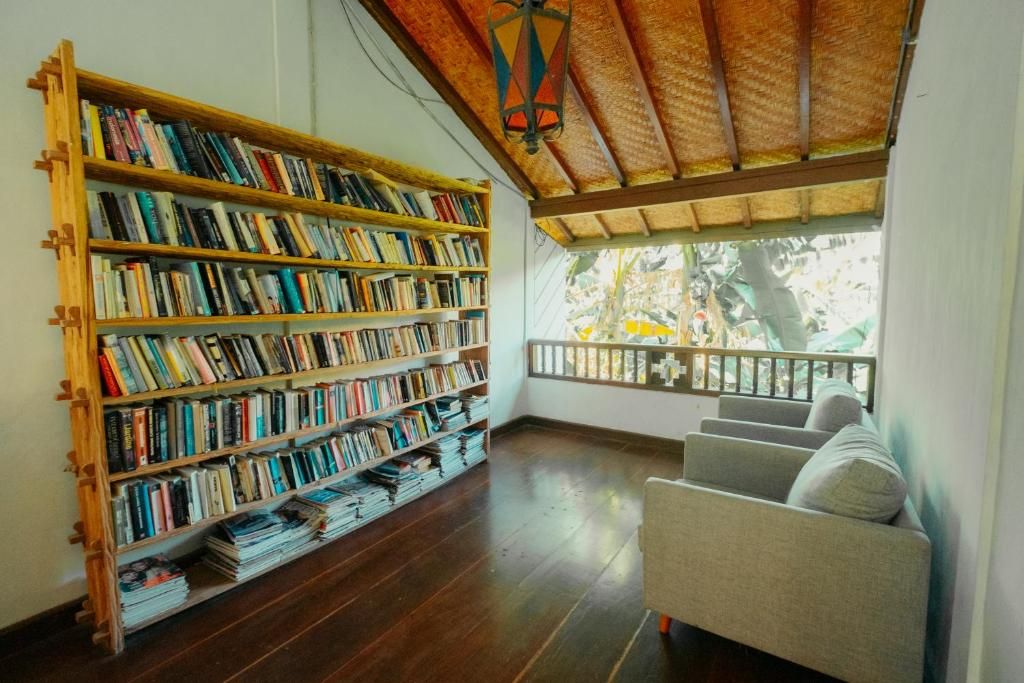 Ein Zimmer mit einer Holzhülle gefüllten Bücherregal, einer gepolsterten Sitzecke und Blick ins Freie durch ein Fenster.