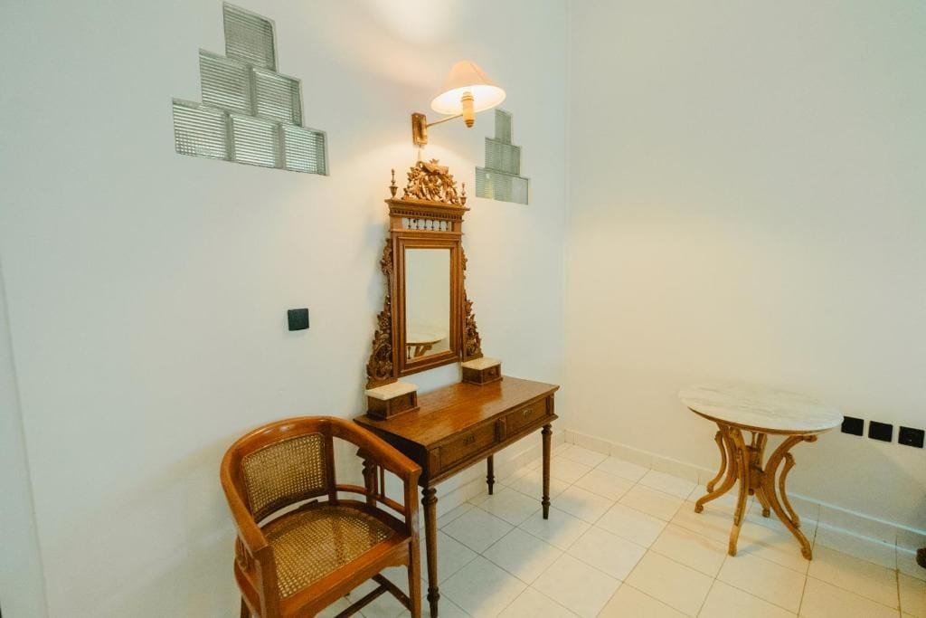 Une pièce comprenant une chaise en bois, une petite table, un miroir avec une lampe et des panneaux décoratifs sur les murs.