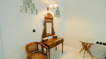 Une pièce comprenant une chaise en bois, une petite table, un miroir avec une lampe et des panneaux décoratifs sur les murs.