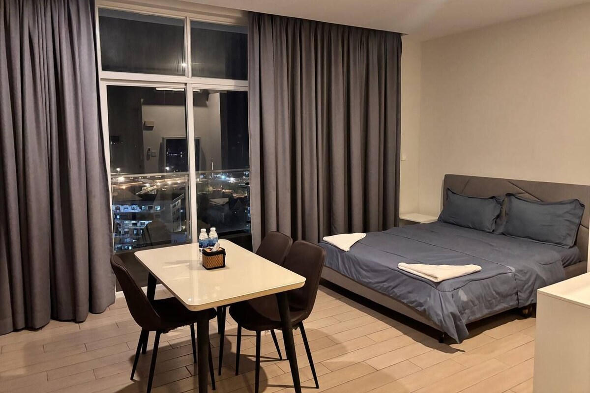 A hotel room with a bed, a dining table with chairs, a window with curtains, and a city view.