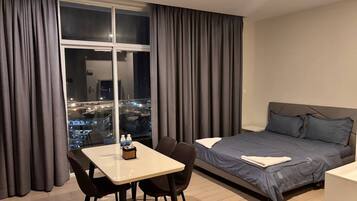 A hotel room with a bed, a dining table with chairs, and a large window with curtains.