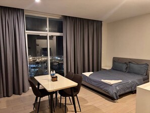 Ein Hotelzimmer mit Bett, Esstisch mit Stühlen, einem Fenster mit Vorhängen und Blick auf die Stadt.