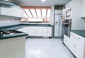 Una cocina con armarios blancos, estufa a gas, horno y refrigerador.