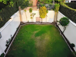 Un espacio exterior rectangular con césped verde, rodeado por un muro blanco y una cerca de metal.