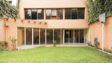 Un edificio de dos pisos con techo plano, grandes puertas correderas de vidrio y un pequeño jardín.