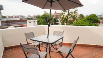 Un patio con una mesa, cuatro sillas, una sombrilla y vistas a edificios y árboles al fondo.