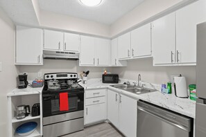 A compact kitchen with white cabinets, a stove, a microwave, a sink, and a dishwasher.