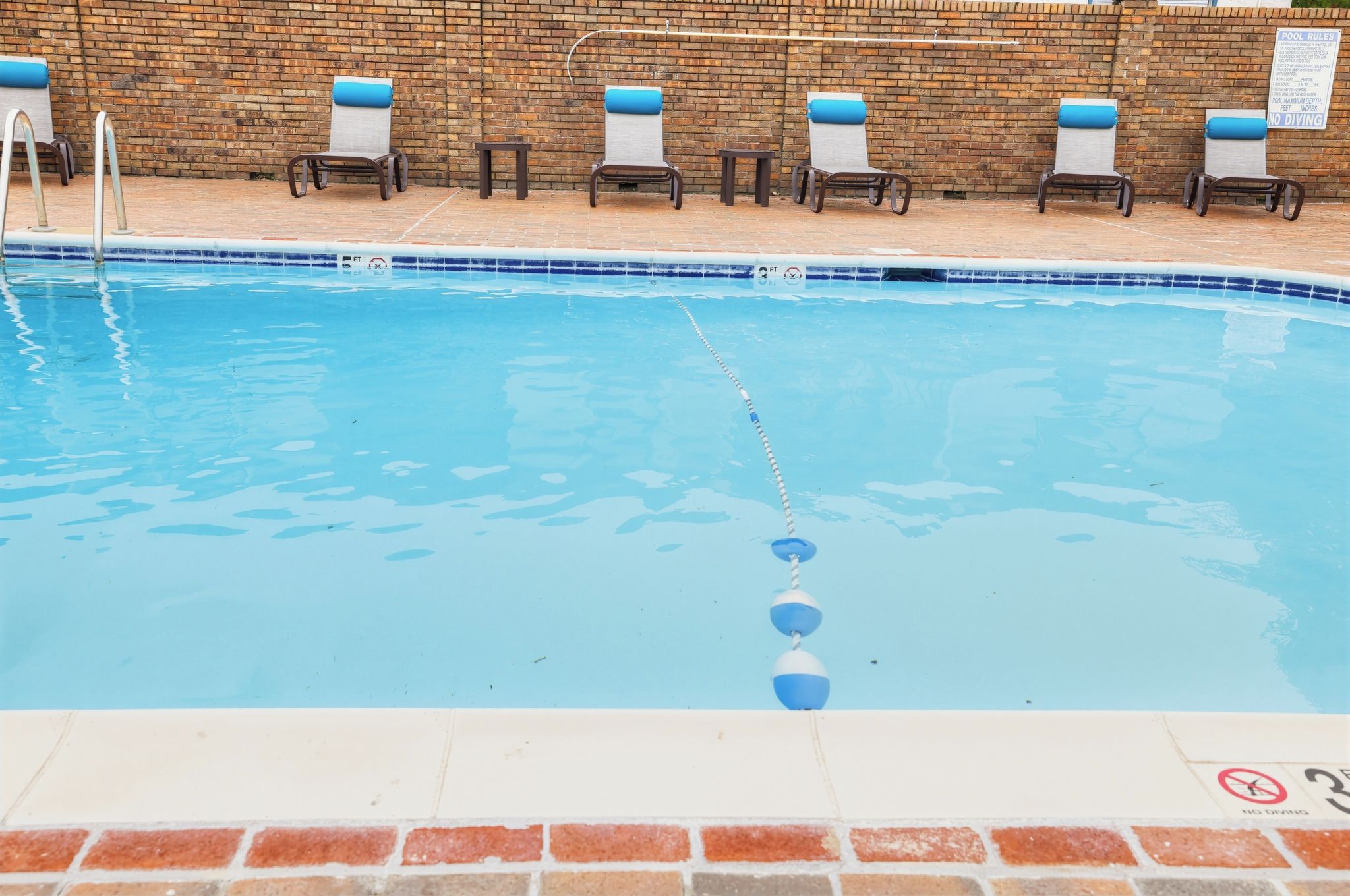 A swimming pool with a brick wall, lounge chairs, and a pool rule sign.