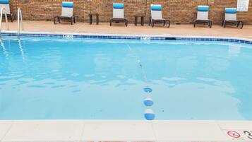 A swimming pool with a brick wall, lounge chairs, and a pool rule sign.
