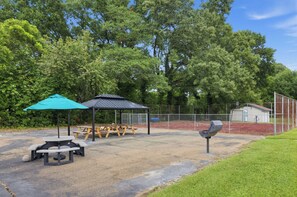 Ein Spielplatz mit Picknicktischen, einer überdachten Sitzgelegenheit und einem eingezäunten Sportplatz.
