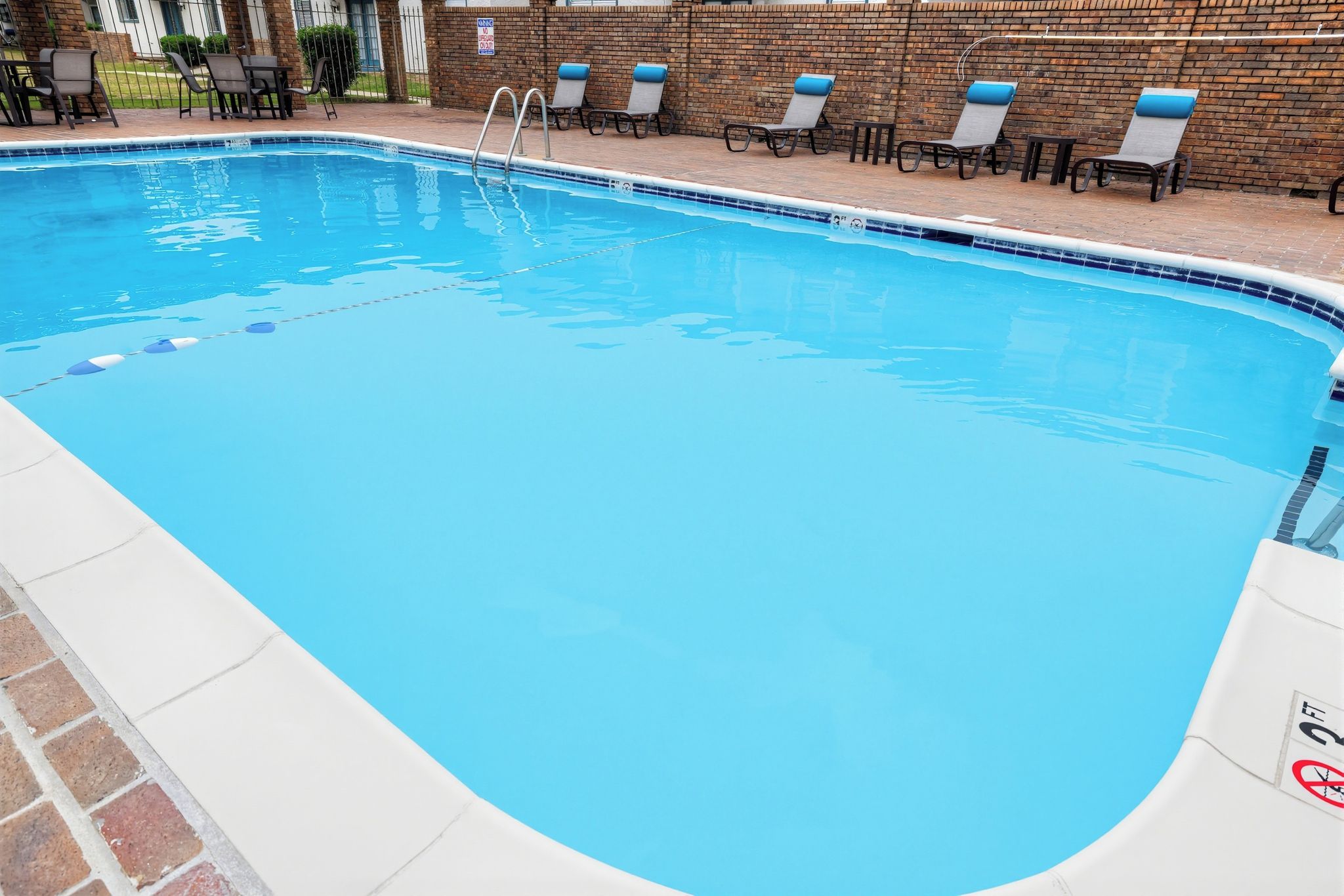 Una piscina con borde de baldosas, un muro de ladrillo y varias sillas de descanso.