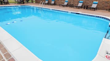 Una piscina con borde de baldosas, un muro de ladrillo y varias sillas de descanso.