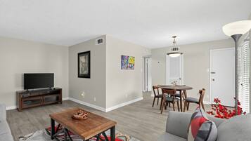 A living room with a sofa, a coffee table, a TV, and a dining area with chairs and a table.