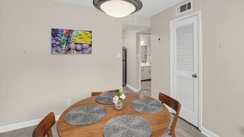 A dining area with a round wooden table, four chairs, a vase with flowers, and a ceiling light fixture.